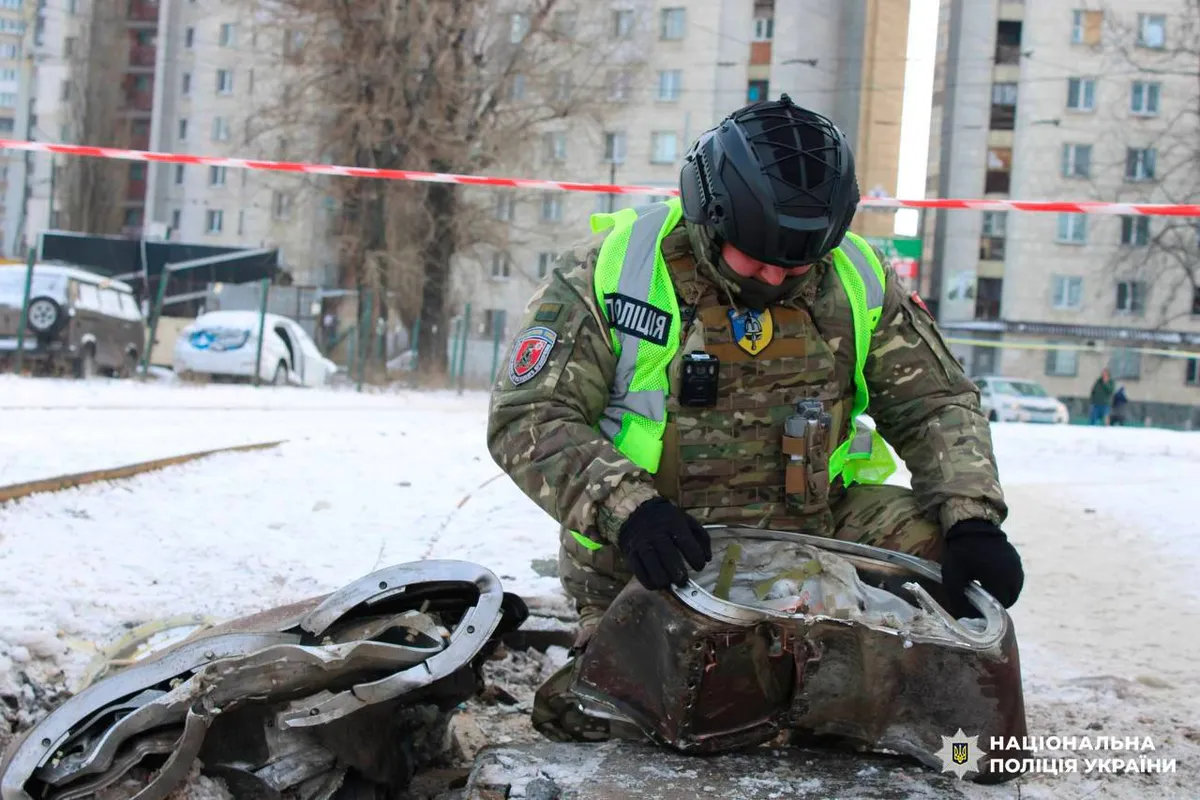 Сапер поліції в шоломі оглядає покручені уламки ракети на снігу у дворі багатоповерхівок